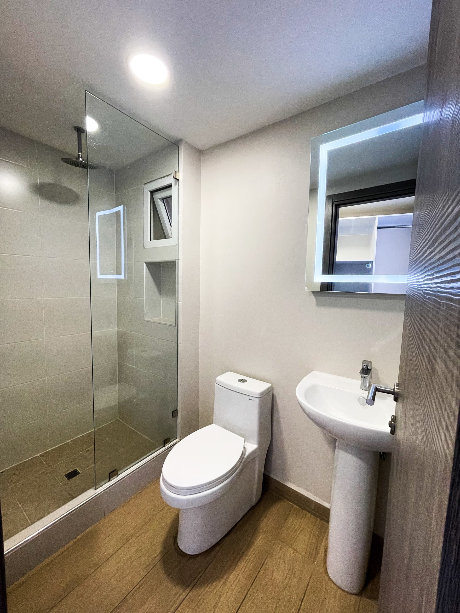 Baño con ducha, inodoro y lavamanos con espejo iluminado